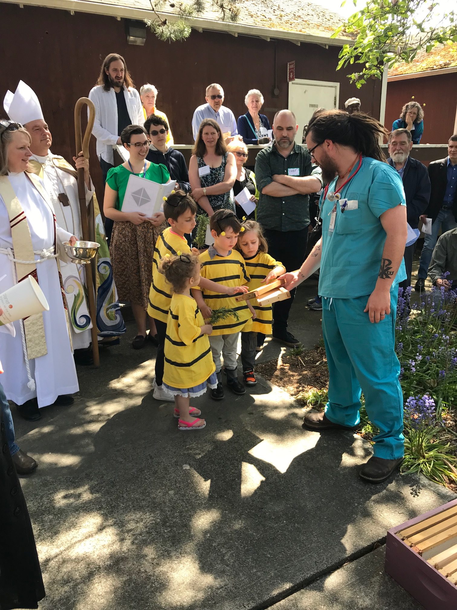 scene with crowd of people and a group of four kids in the center wearing yellow shirts with black stripes to look like bees.