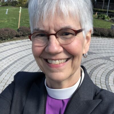 image of older woman smiling with short grey hair and glasses wearing clerical collar