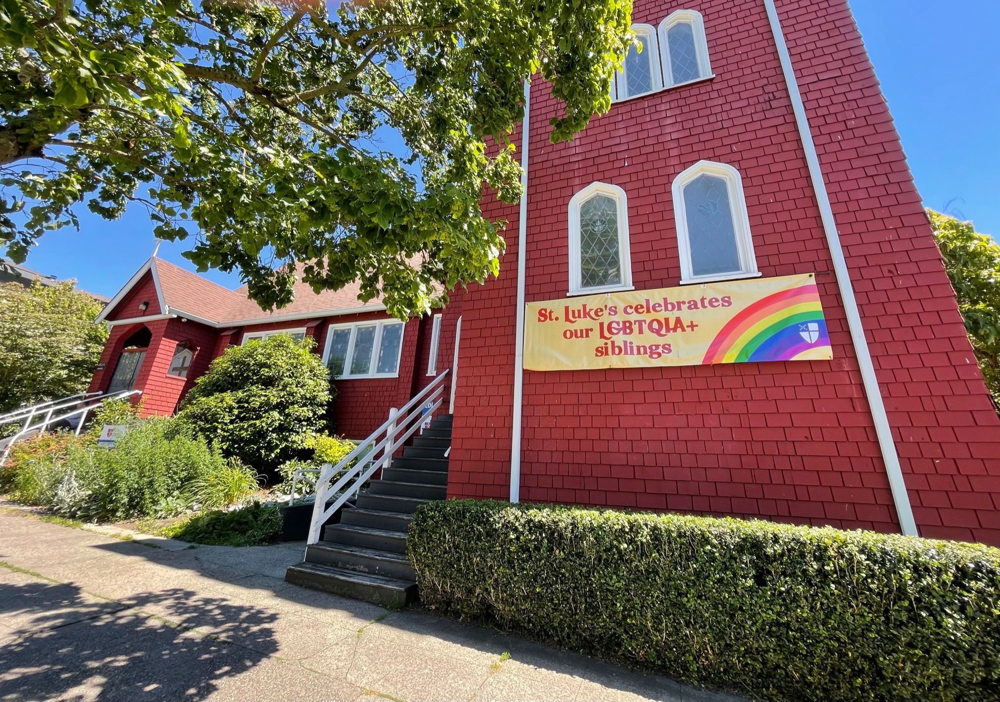image of a red chapel with a banner stating St. Luke's celebrates our LGBTQIA+ siblings