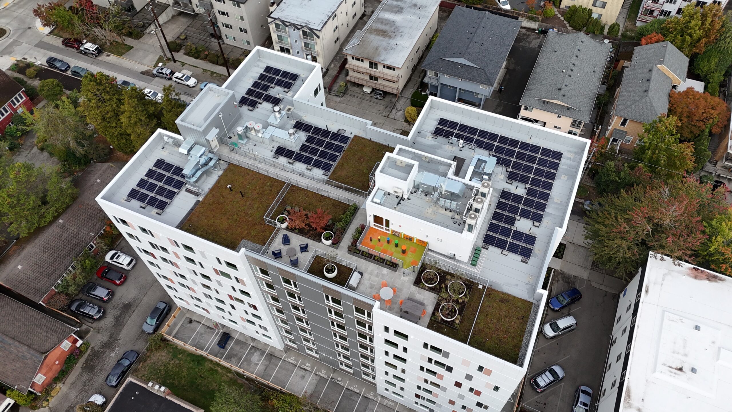 birdseye view of an apartment building rooftop with solar panels, garden space, and play area
